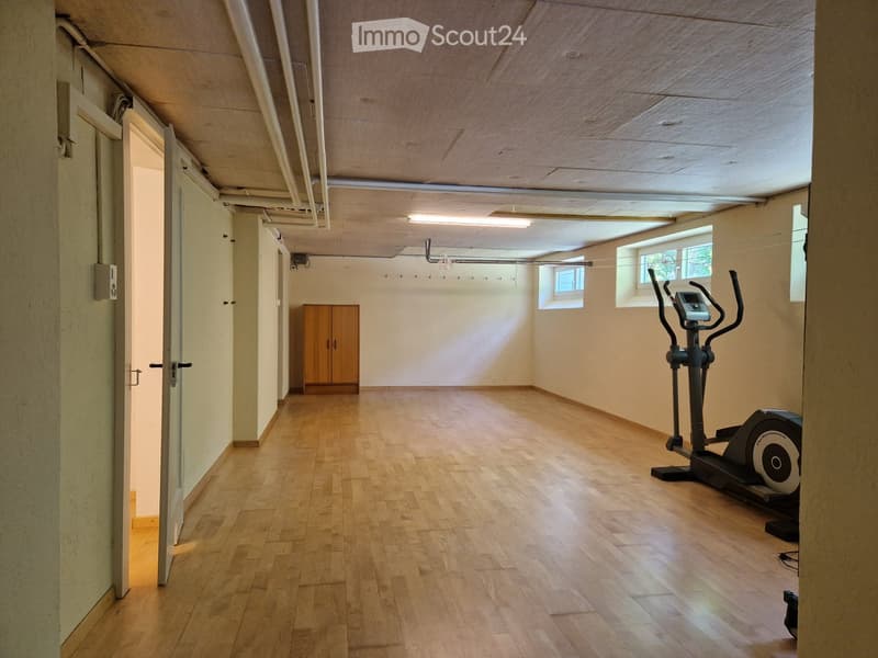 Exercise room with wooden flooring, exercise bike, and a small wooden cabinet.