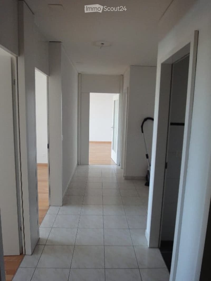 Tiled hallway with white walls and wooden floor, open doors, empty hallway