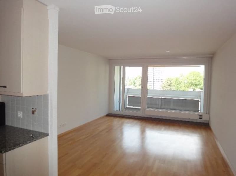 Empty room with wooden floors, white walls, large sliding glass doors to a balcony, white cabinets.