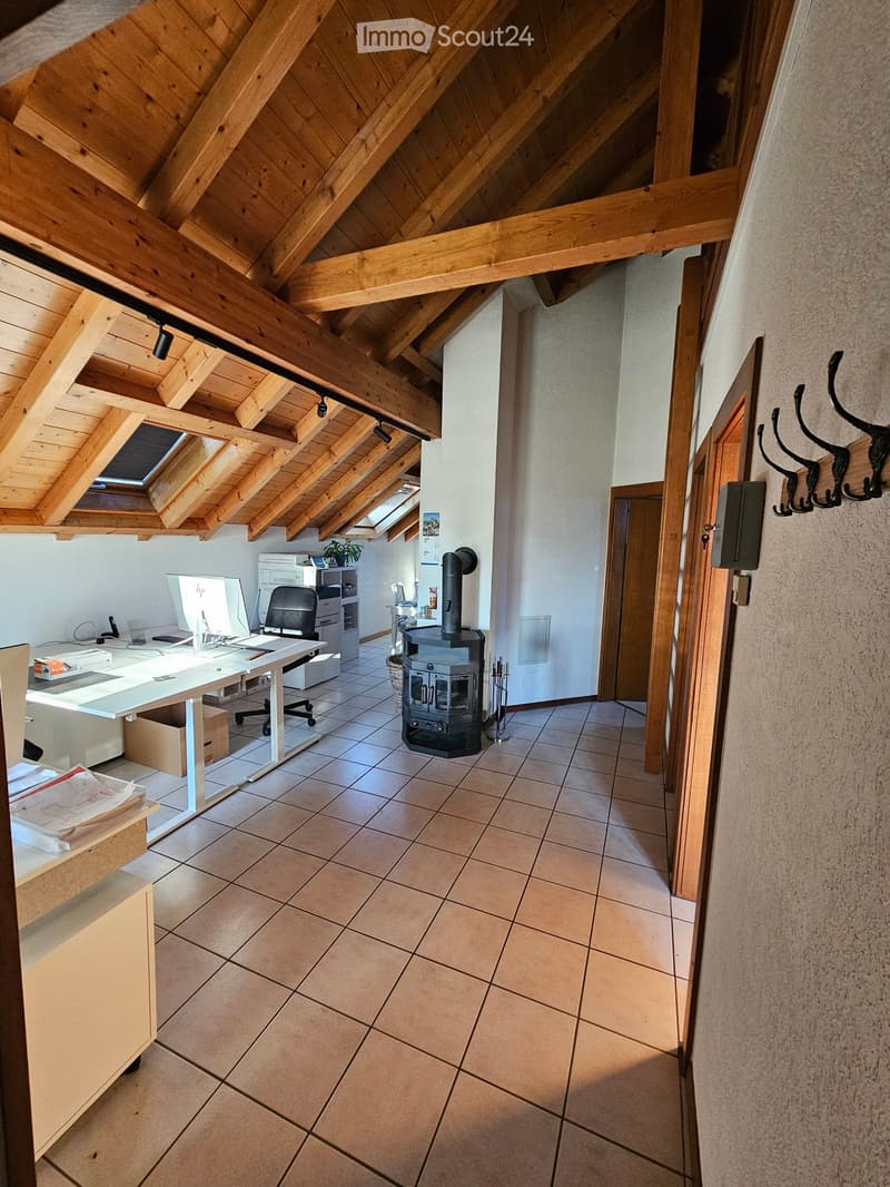 Office space with a wooden slanted ceiling, tiled floor, desk with computer, chair, printer, and a small fireplace.