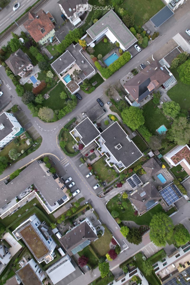 Aerial view of a residential neighborhood with multiple houses, gardens, driveways, and parked cars.