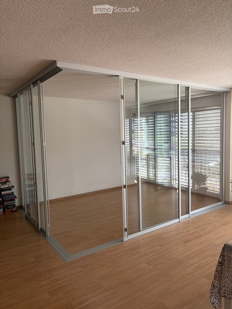 Modern interior with large sliding glass doors, wooden flooring, and a small table with books near the entrance.