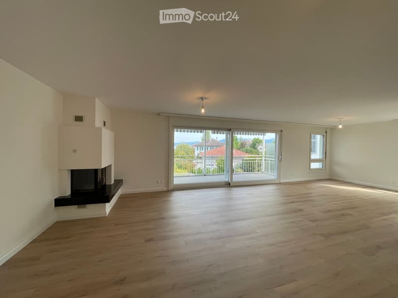 Empty room with wooden flooring, white walls, large sliding glass doors leading to a balcony, and a fireplace on the left side.