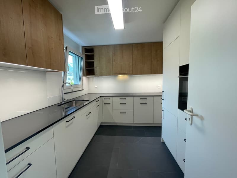 Modern kitchen with white cabinets, dark countertops, and a stainless steel sink. Features include a window, built-in cabinets, and a sleek design.