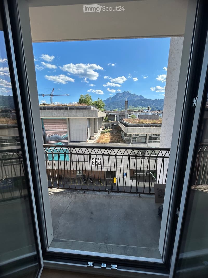 Balcony with metal railing, overlooking a parking area and distant mountains under a clear blue sky.