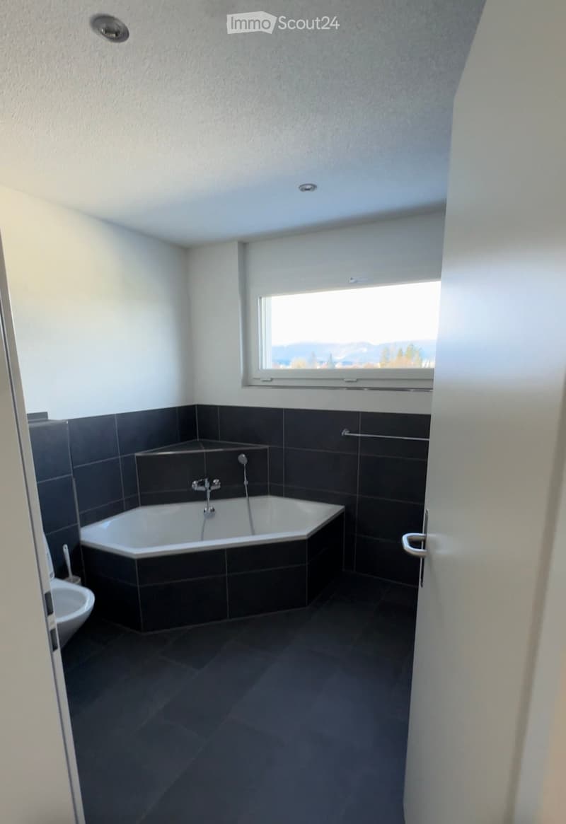 modern bathroom, bathtub, toilet, window with mountain view, tiled walls and floor, shower area with metal rack