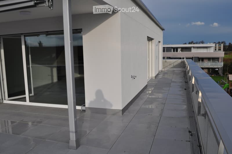 A balcony of a white apartment building with gray tiled flooring and glass doors.