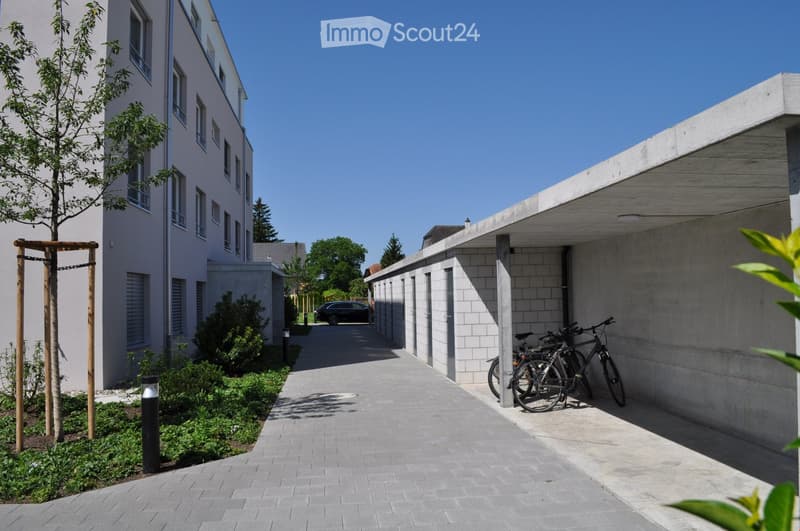 Two story building with multiple windows, a covered parking area with bicycles parked, and a small green patch at the bottom.