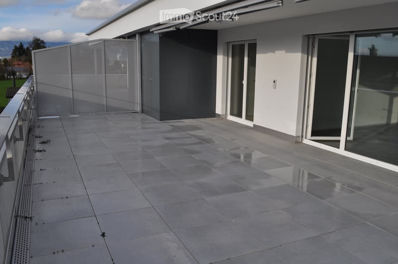 Balcony with gray tiles, metal railings, entrance gate, sliding glass doors, white exterior wall, mountains in background
