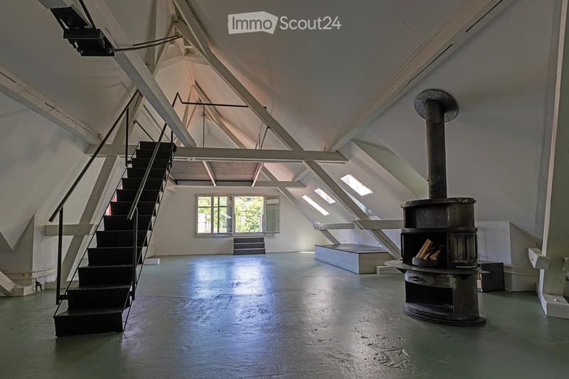 Empty attic space with exposed wooden beams, a metal staircase, a large window, and a wood-burning stove.