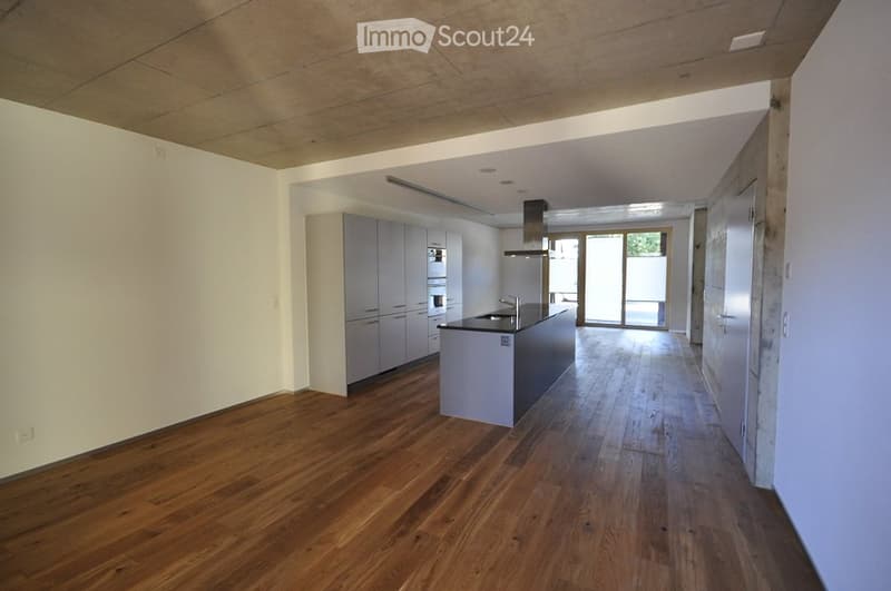 Modern, unfurnished kitchen with light grey cabinets, a central island, and wooden flooring. The space features a sleek design with a large window offering natural light.