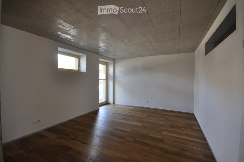 Empty room with wooden flooring, white walls, and large windows allowing natural light. No furniture or equipment present.