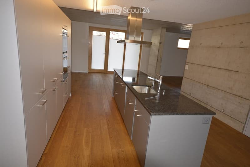 Modern kitchen with light-colored cabinets, stainless steel sink, and a range hood. The floor is wooden, and there is a sliding glass door leading to another room.