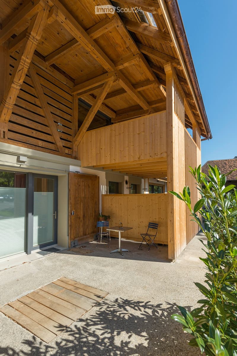 Wooden outdoor seating area with a table and two chairs, surrounded by wooden structures and greenery.