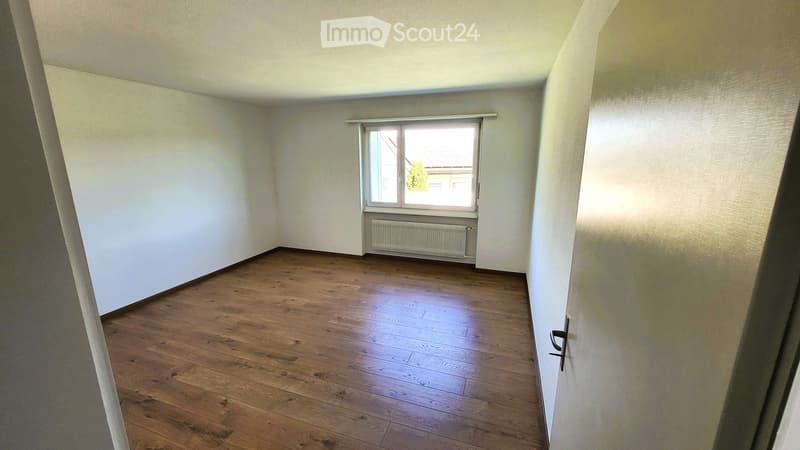 Empty room with wooden flooring, white walls, and a single window with a radiator below it.