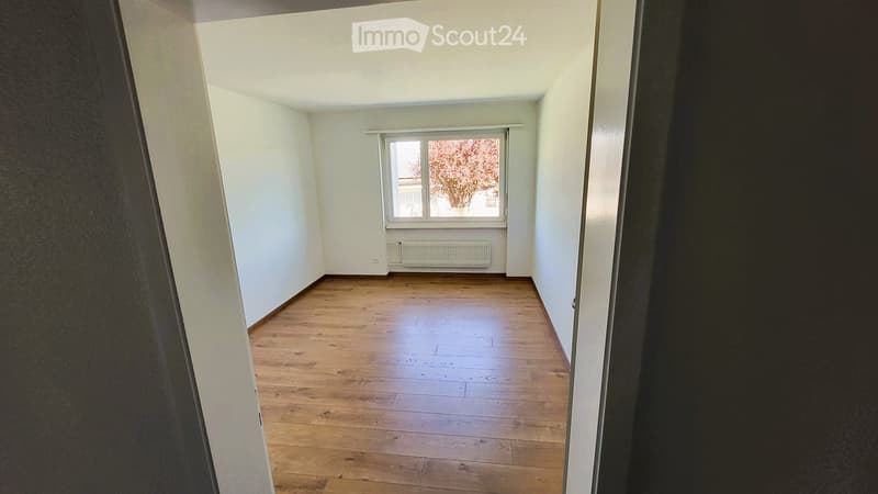Empty room with wooden flooring, white walls, and a single window with a radiator below it.