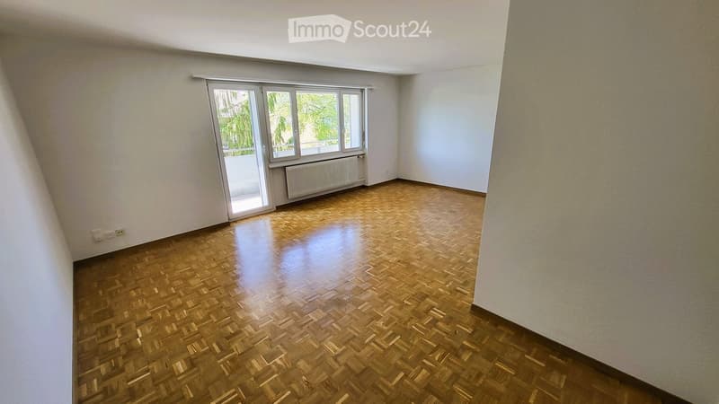 Empty room with wooden parquet flooring, white walls, large window with blinds, radiator, and power outlets.