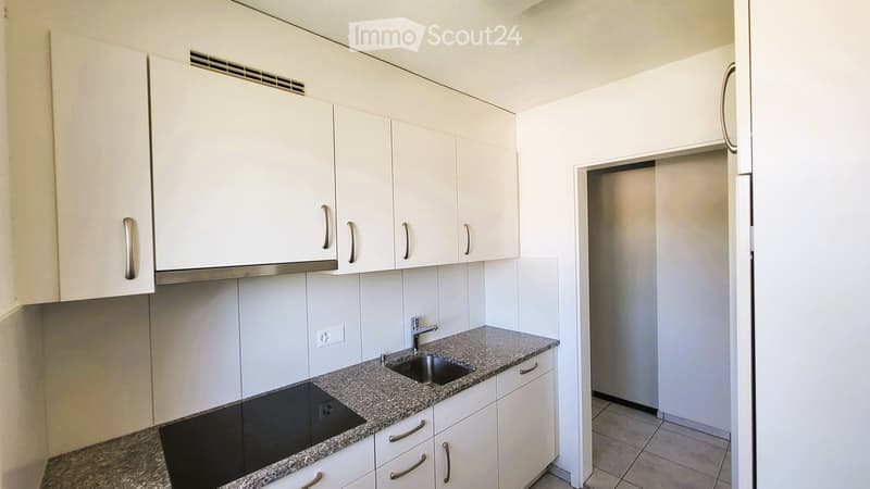 Modern kitchen with white cabinets, granite countertop, sink, and electric stove. The space is clean and well-lit with tiled flooring.