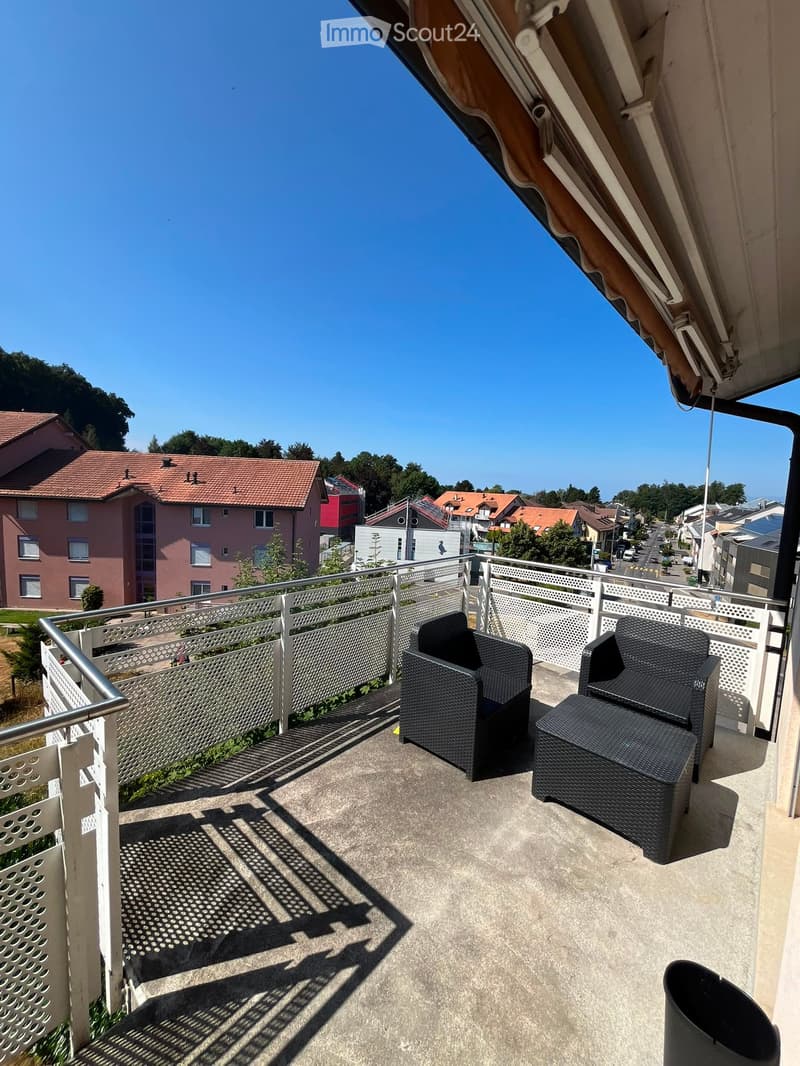 Balcony with two black wicker chairs and a matching table, metal railing, and a view of the neighborhood.