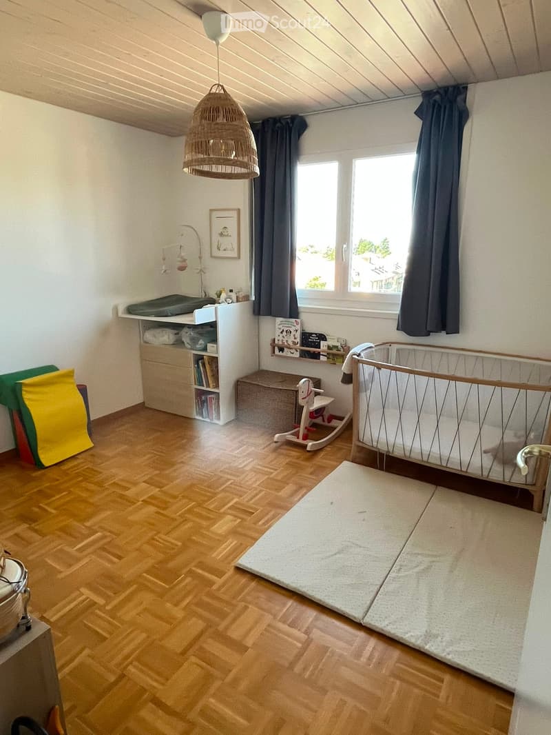 Brightly lit children's bedroom with wooden flooring, a crib, changing table, bookshelf, toy rocking horse, and a play mat.