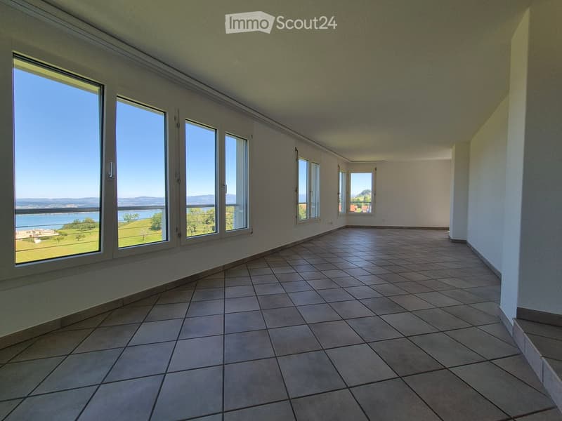 Empty room with tiled floor, large windows offering a scenic view of a lake and surrounding landscape.