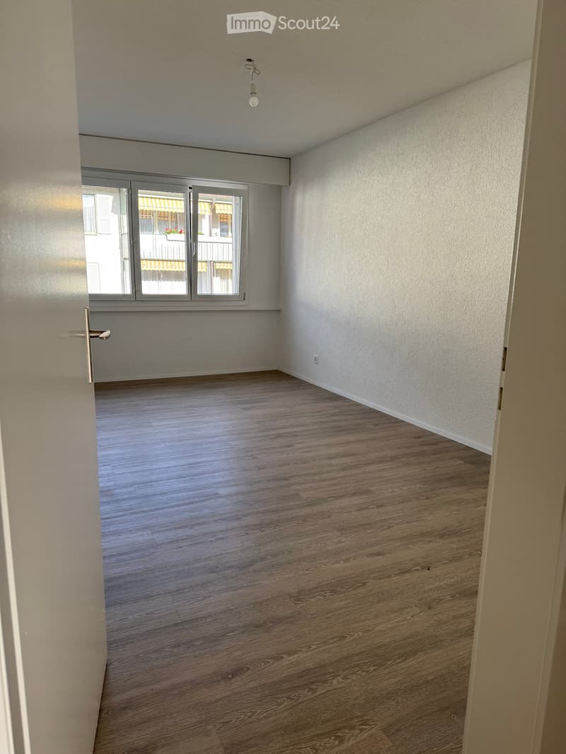 Empty room with wooden flooring, white walls, and a large window with a view of a balcony area.