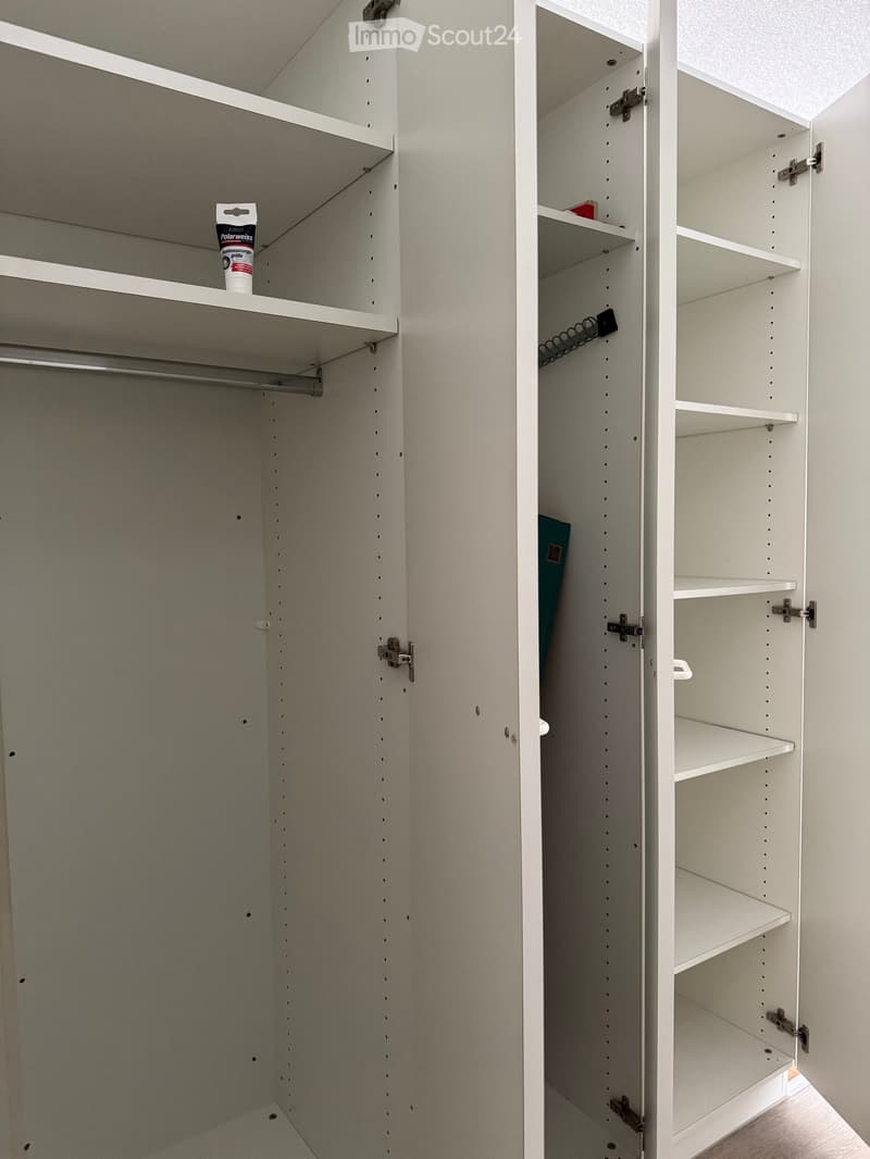 Empty closet with white shelves and a hanging rod, featuring a few small items on the top shelf.