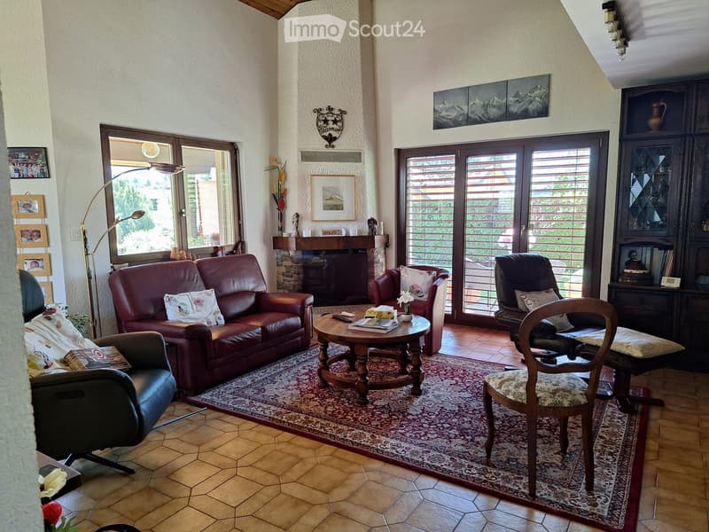 Living room with a red leather sofa, armchairs, coffee table, fireplace, and large windows with a view.