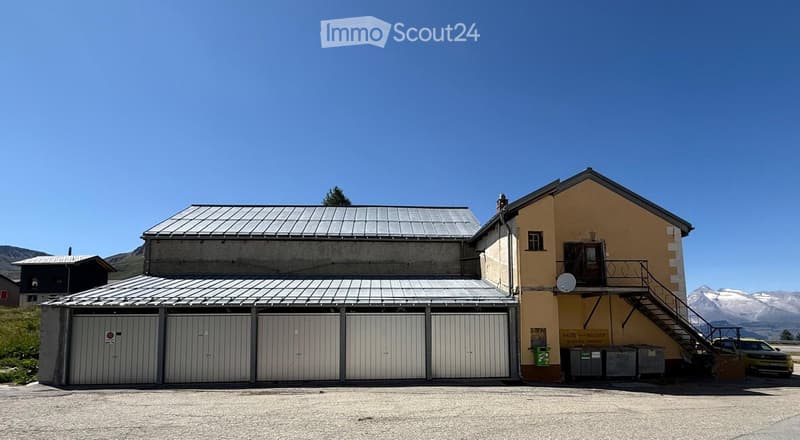 Two-story building with a garage section and a yellow-painted main structure, set against a mountainous backdrop.
