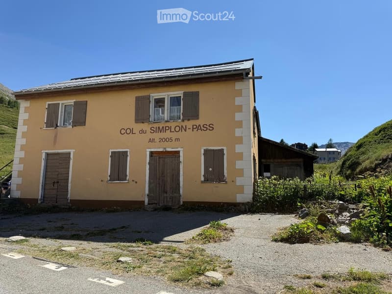 Two-story building with yellow walls, brown shutters, and a metal roof, labeled "COL du SIMPLON-PASS" with an altitude of 2005 m.