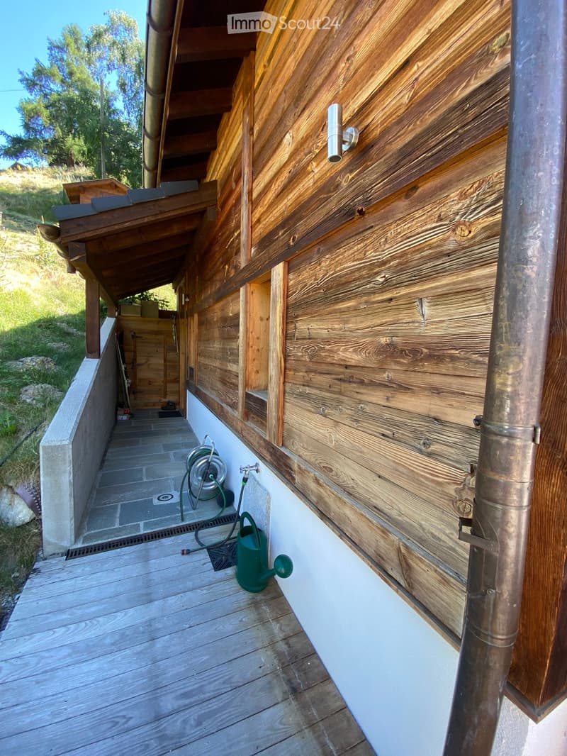 Wooden balcony with a covered section, tiled pathway, and garden hose reel.