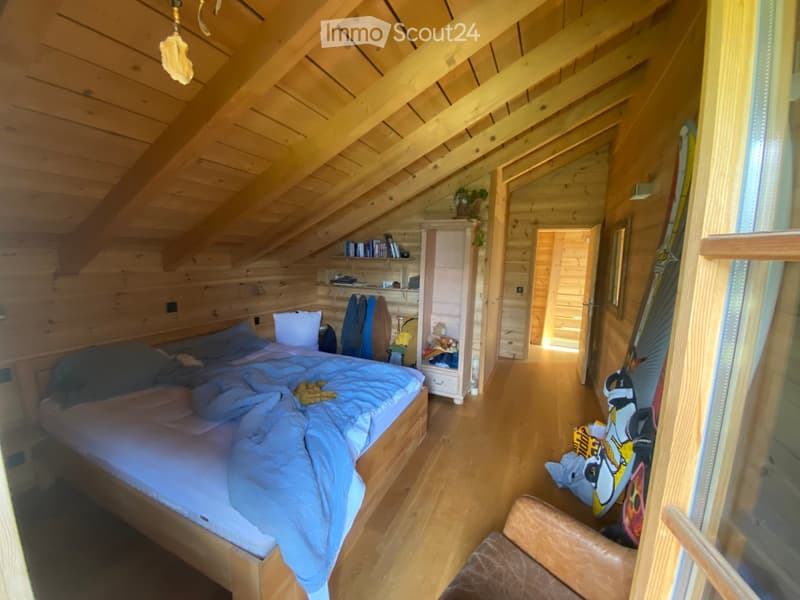 Cozy wooden bedroom with slanted ceilings, a bed with blue bedding, a small bookshelf, a chair, and a mirror on the wall.