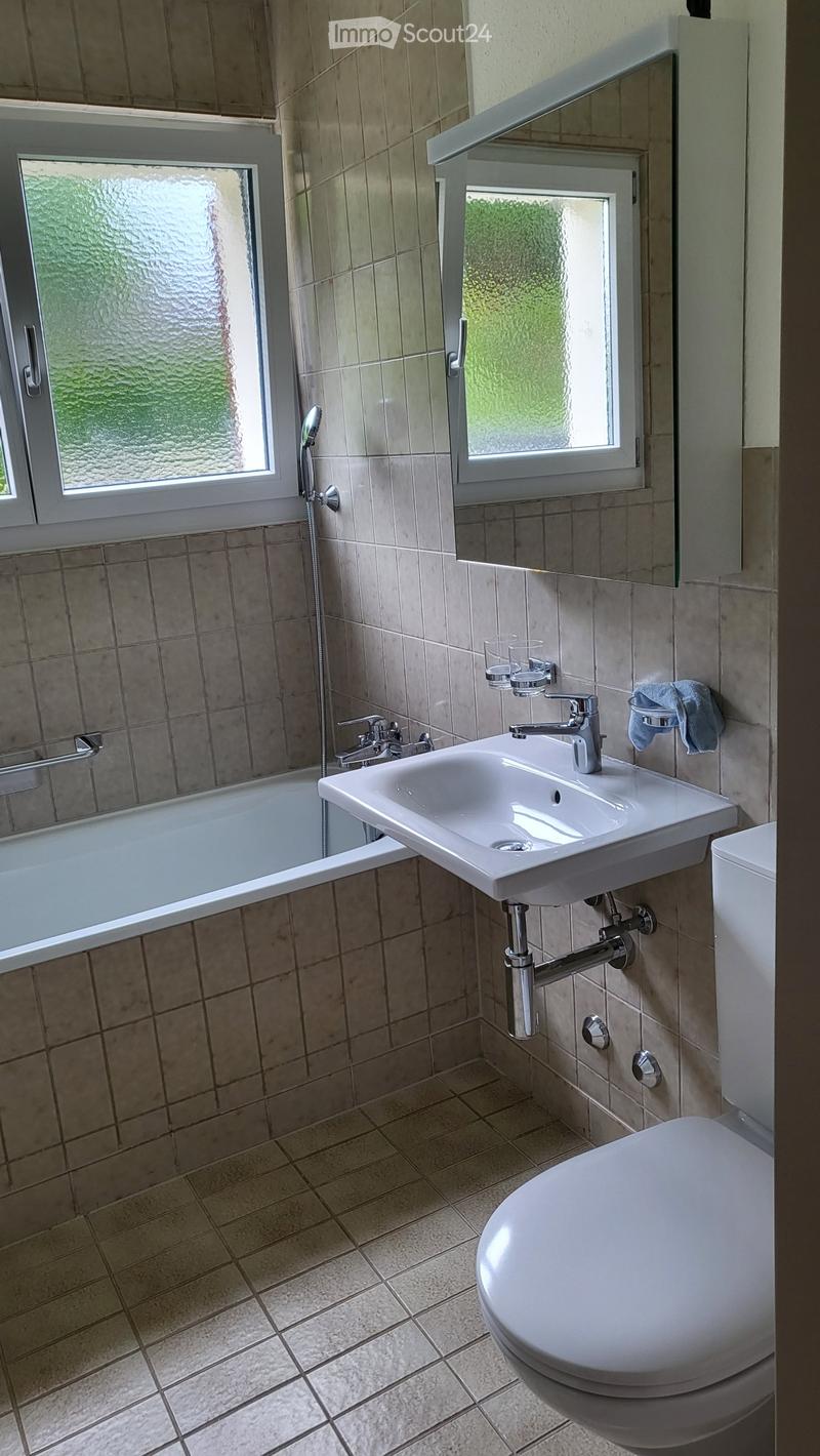 Bathroom with beige tiled walls and floor, white sink, toilet, bathtub, and a mirror above the sink.