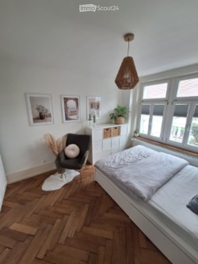 Cozy bedroom with wooden flooring, a double bed, a single chair, a mirror, and a hanging lamp.
