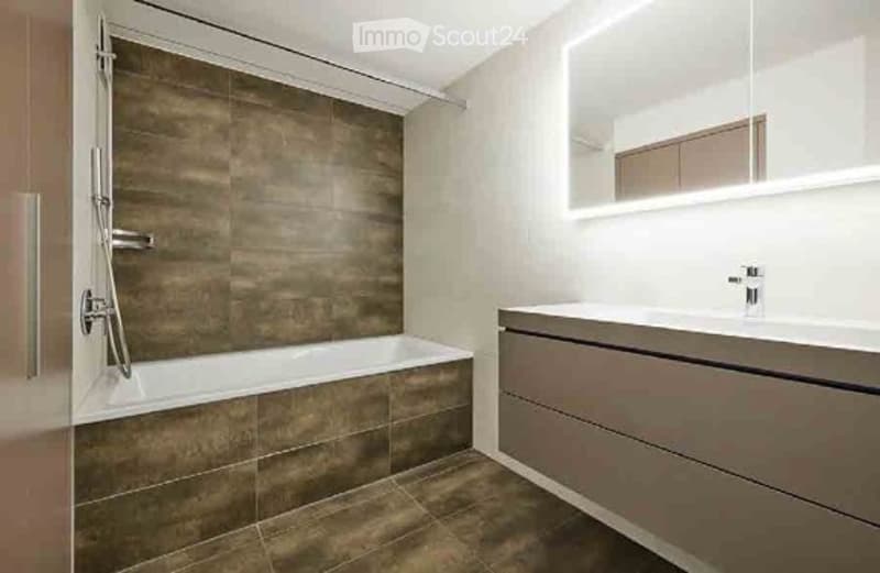 Modern bathroom with a bathtub, sink, and mirror. The walls are tiled in a dark brown color, and the floor is also tiled in a matching dark brown color. The sink has a sleek, modern design with a chrome faucet.