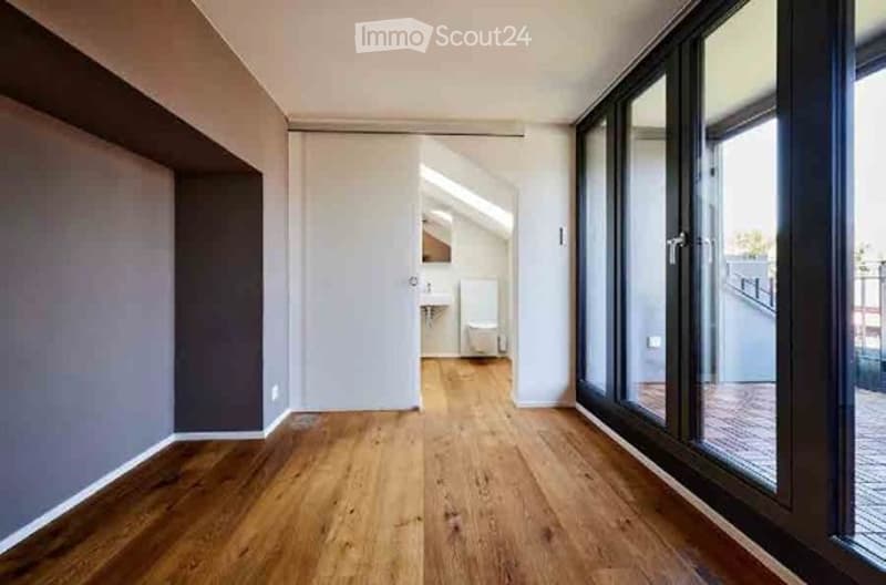 Empty room with wooden flooring, large windows, and a view to a balcony area. No furniture or equipment present.