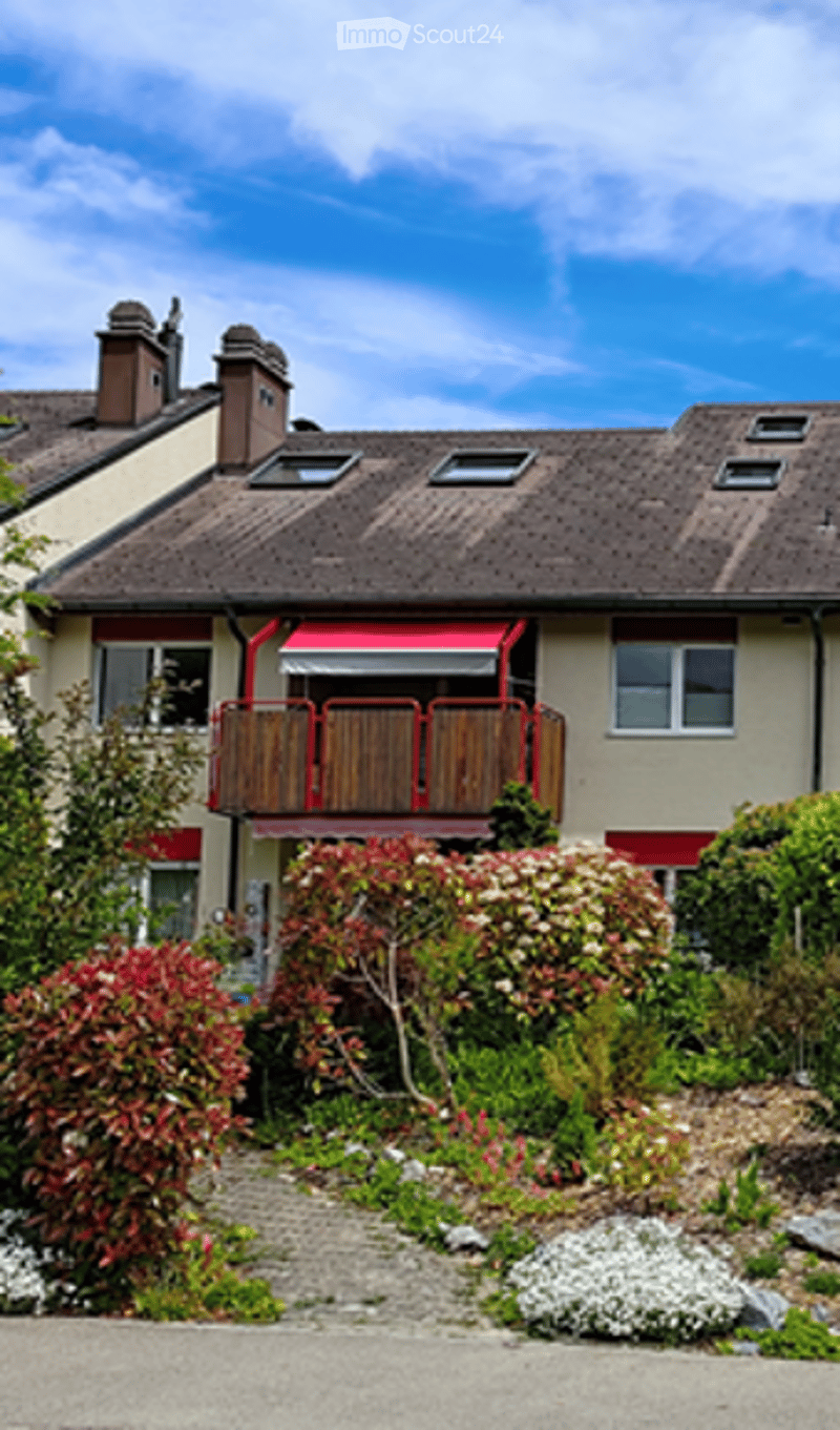Two-story house with a balcony, red awning, and well-maintained garden.