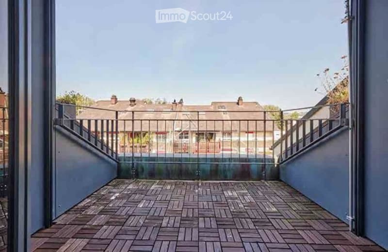 Balcony with wooden decking, metal railing, and view of neighboring buildings.