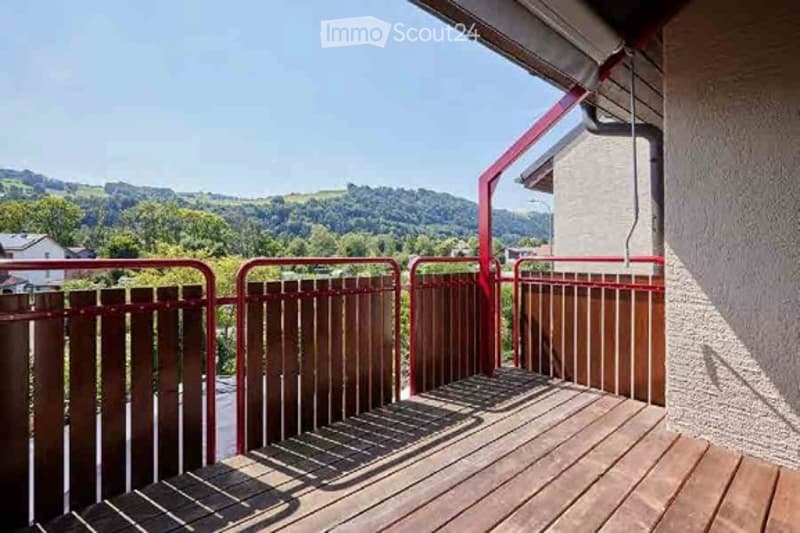 Balcony with wooden decking, red metal railing, scenic mountain view in the background.