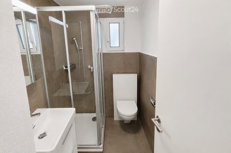 Modern bathroom with a bathtub, toilet, and glass-enclosed shower stall. The walls are tiled in brown and white, and the floor is tiled in brown.