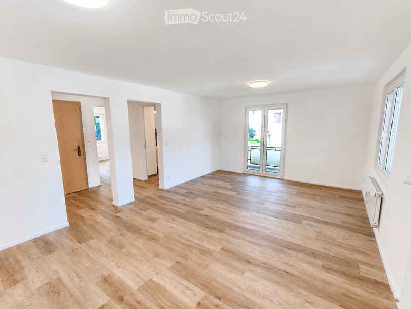 Empty room with light wooden flooring, white walls, and a large sliding glass door leading to a balcony.