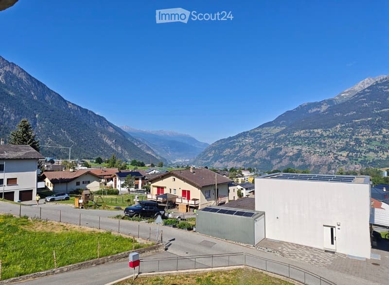 Aerial view of a residential area with houses, parked cars, and a scenic mountain backdrop.