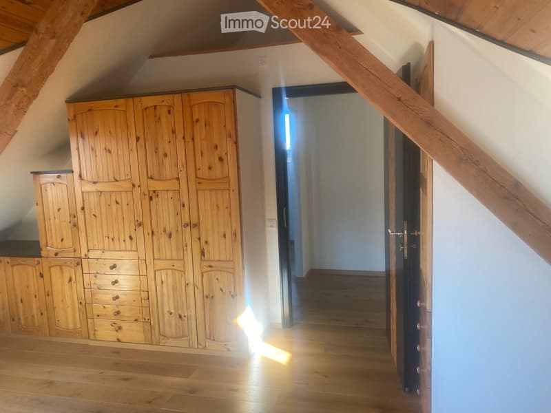 A wooden-floored hallway with a large wooden wardrobe on one side and a staircase leading upwards, featuring exposed wooden beams on the ceiling.