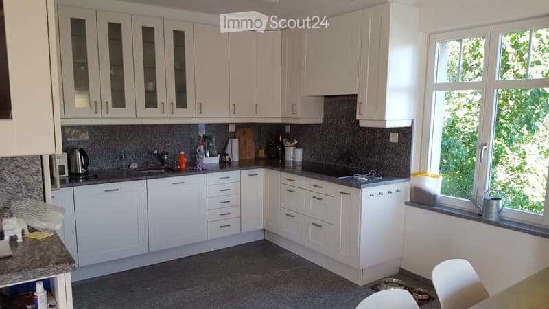 Modern kitchen with white cabinets, granite countertops, and stainless steel appliances. Features include a sink, stove, kettle, and various kitchen items on the counter.