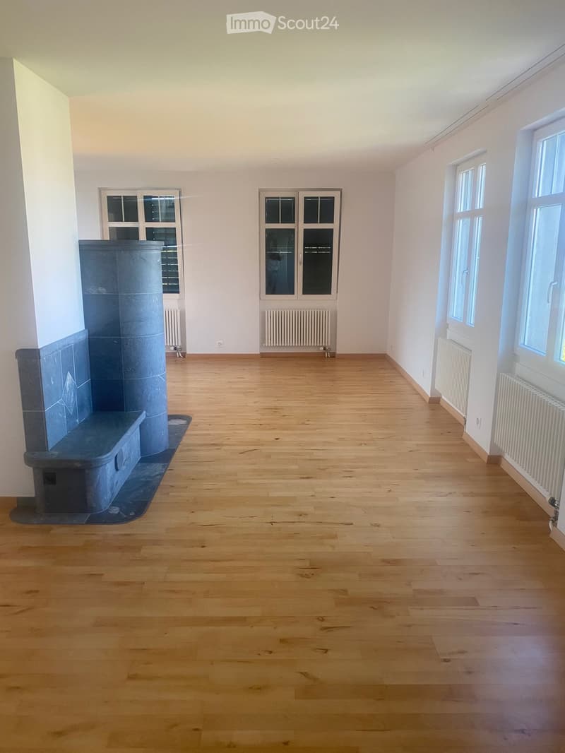 Empty room with wooden flooring, white walls, multiple windows, and a radiator. No furniture or equipment present.