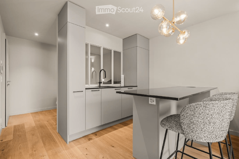 Modern kitchen with grey cabinets, black countertop, island, and two stools. Features a sleek faucet and a contemporary light fixture.