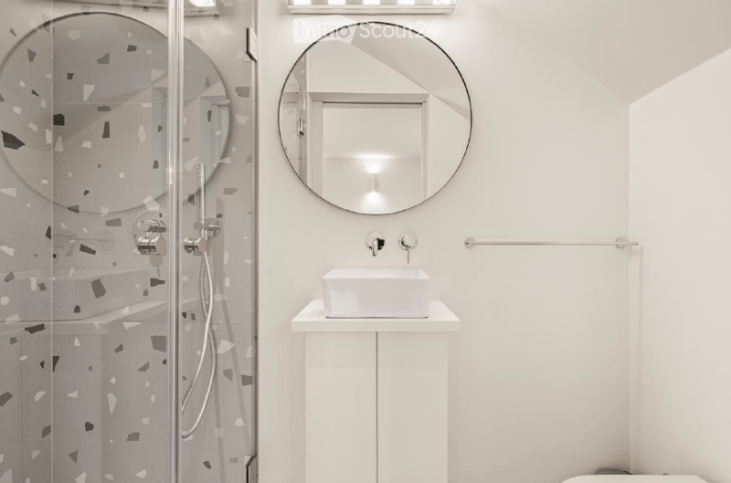 Modern bathroom with a white sink, round mirror, glass shower enclosure with decorative tiles, and a towel rack.