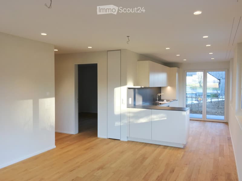 Modern kitchen with white cabinets, a central island, and wooden flooring. Features a large window and recessed lighting.