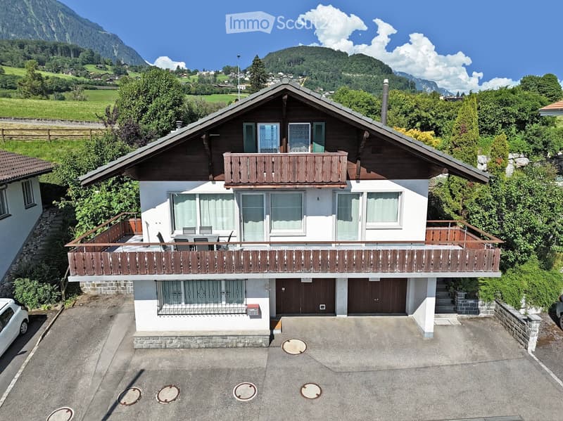 Two-story house with white walls, wooden balconies, and a scenic mountain view in the background.