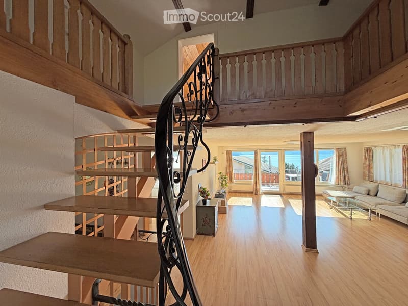 Spacious living room with wooden floors, a staircase with wooden railings and a black wrought iron handrail, a sofa, coffee table, and a small table with a plant.